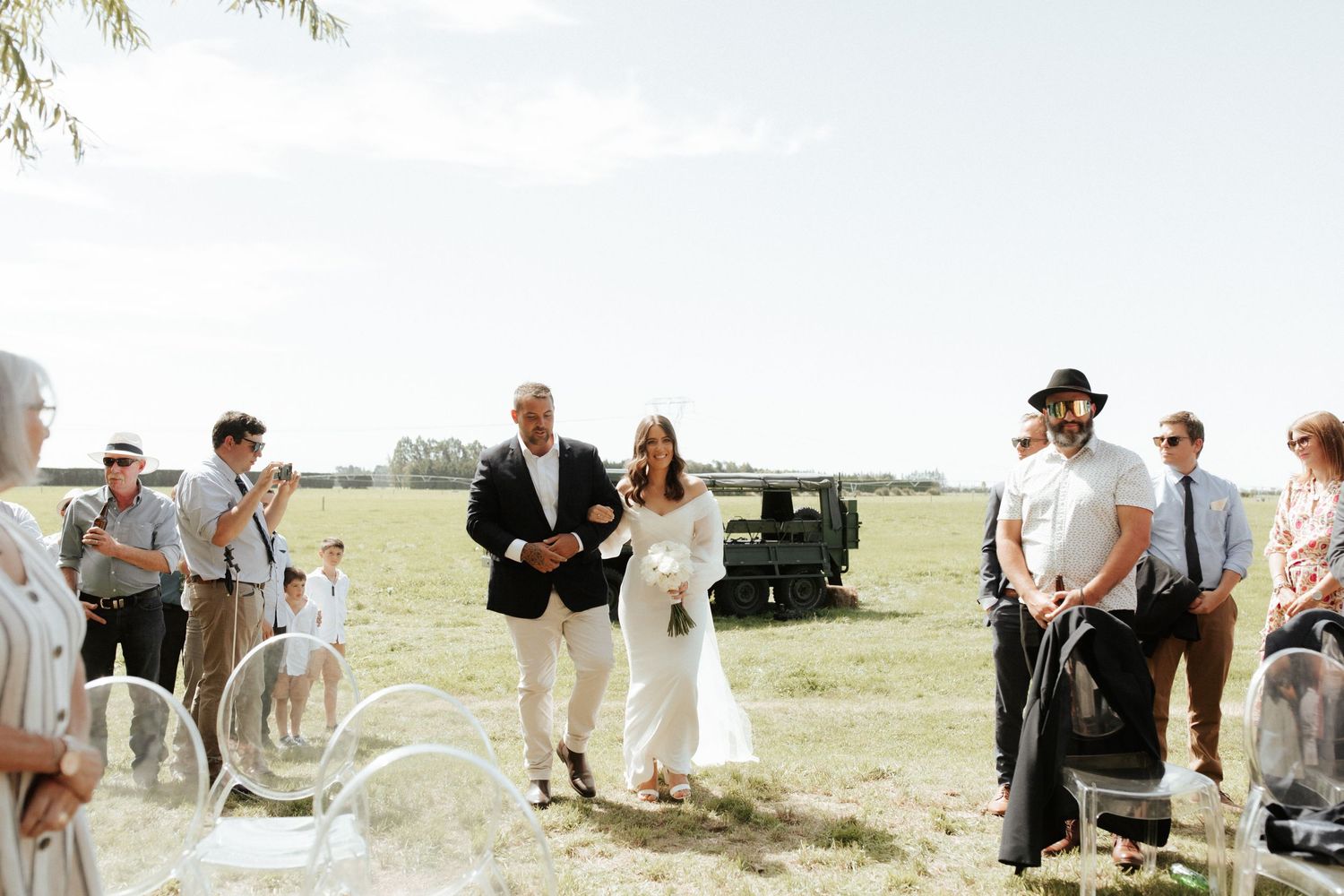Outdoor wedding ceremony in a sunny field with guests watching.