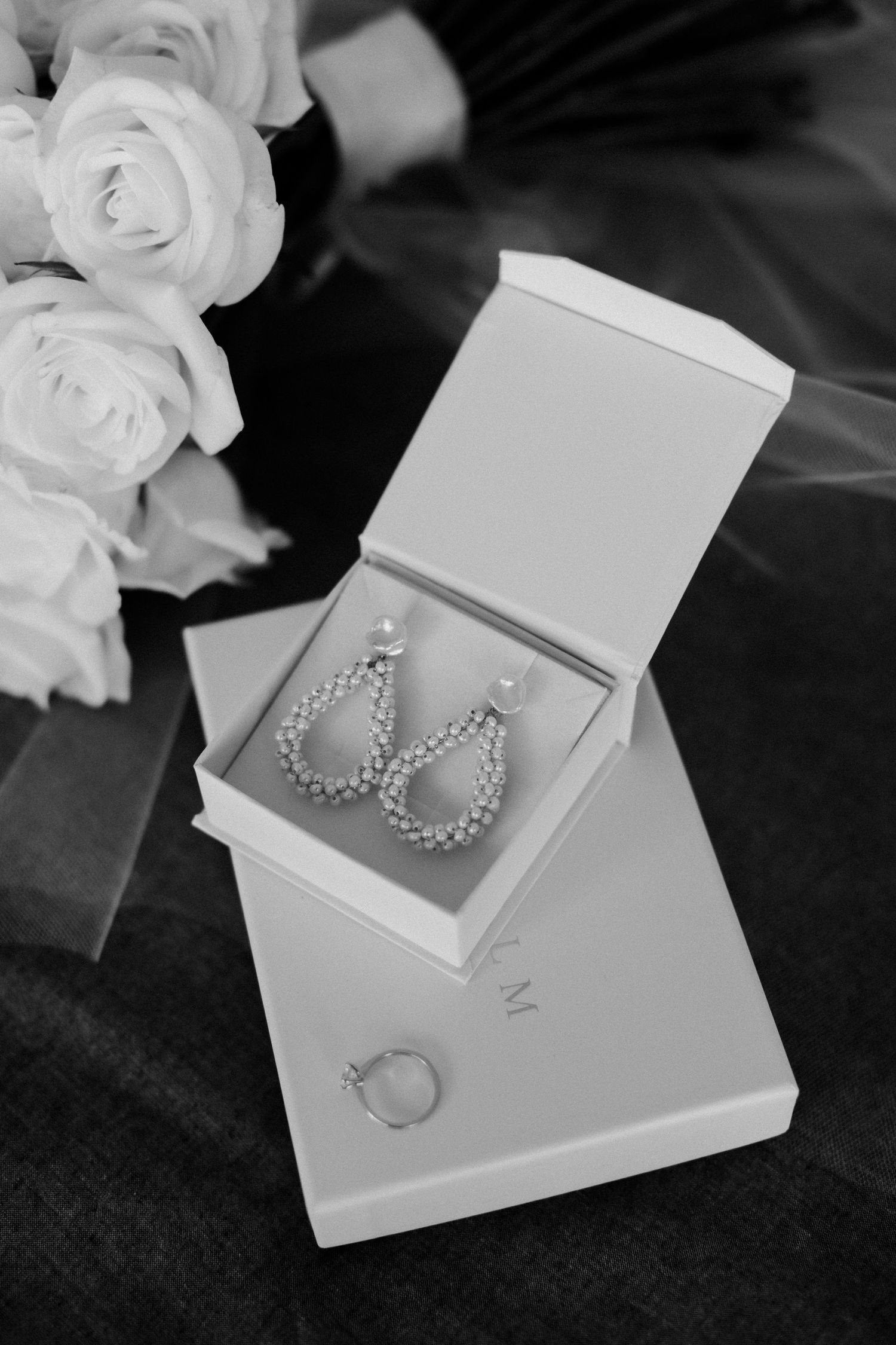 Pearl drop earrings and ring displayed in white jewelry box next to white roses in black and white.