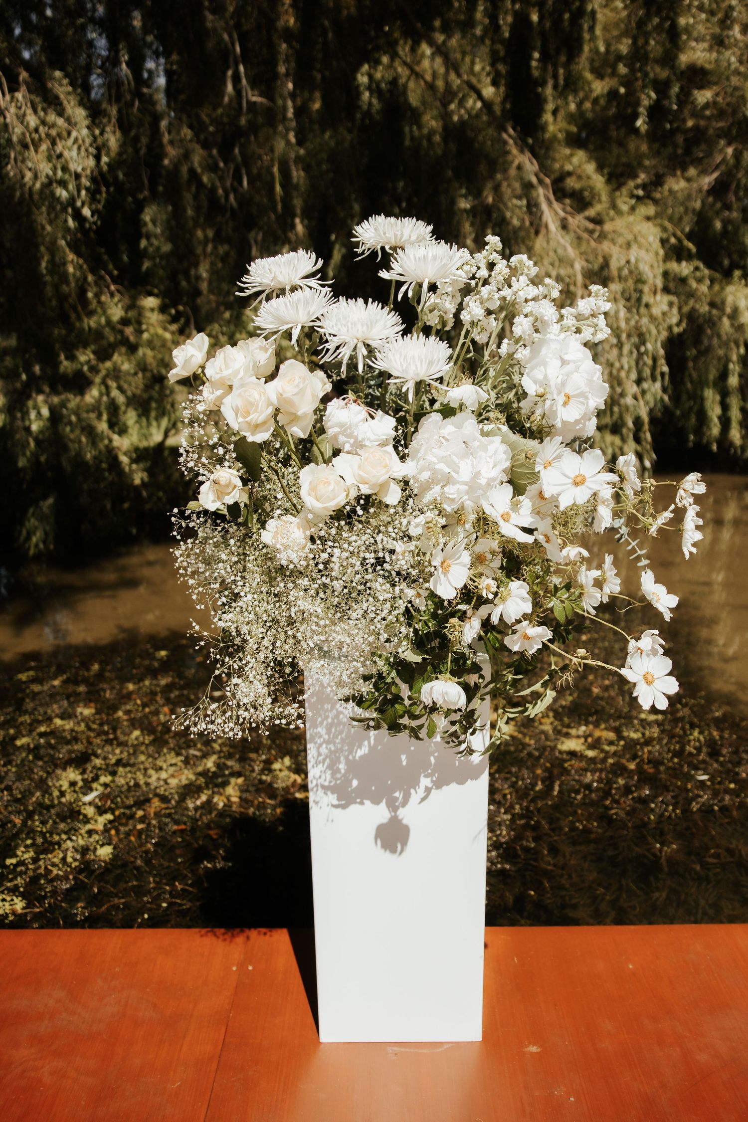 White floral arrangement with baby's breath in a modern vase against dark background.