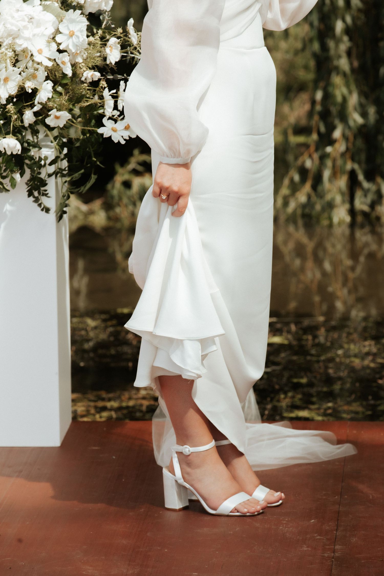 Close-up of bride's white block heel sandals and flowing dress hem.