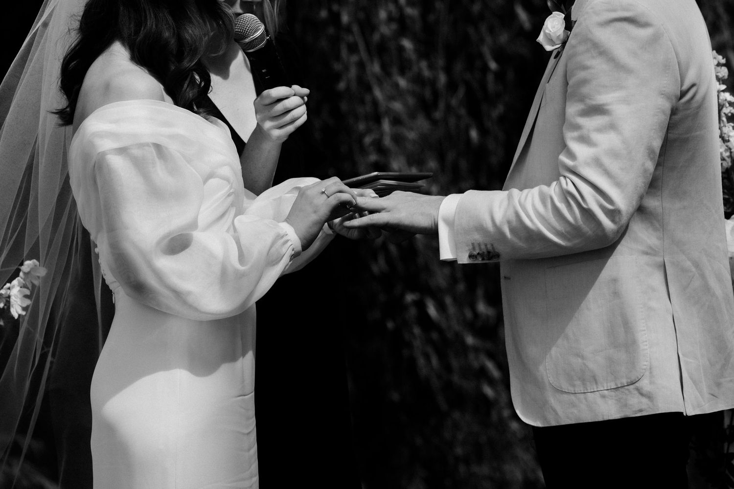 Black and white close-up of wedding ring exchange during ceremony.