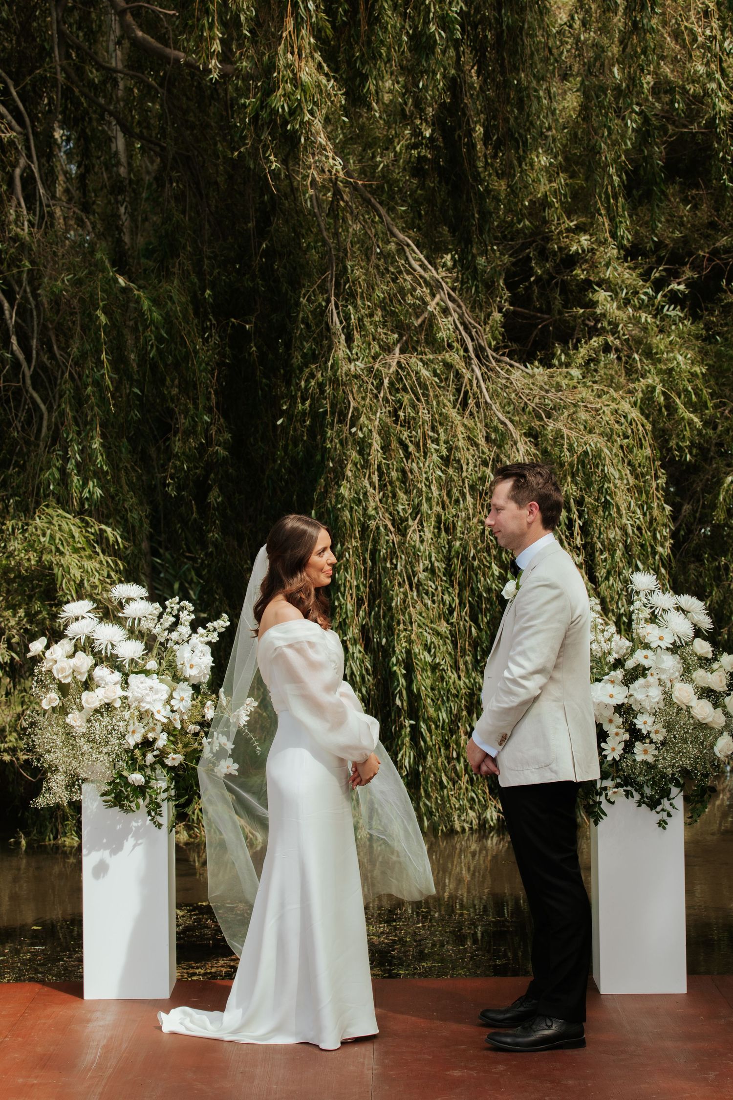 Elegant wedding ceremony setup with white flowers and weeping willow backdrop.