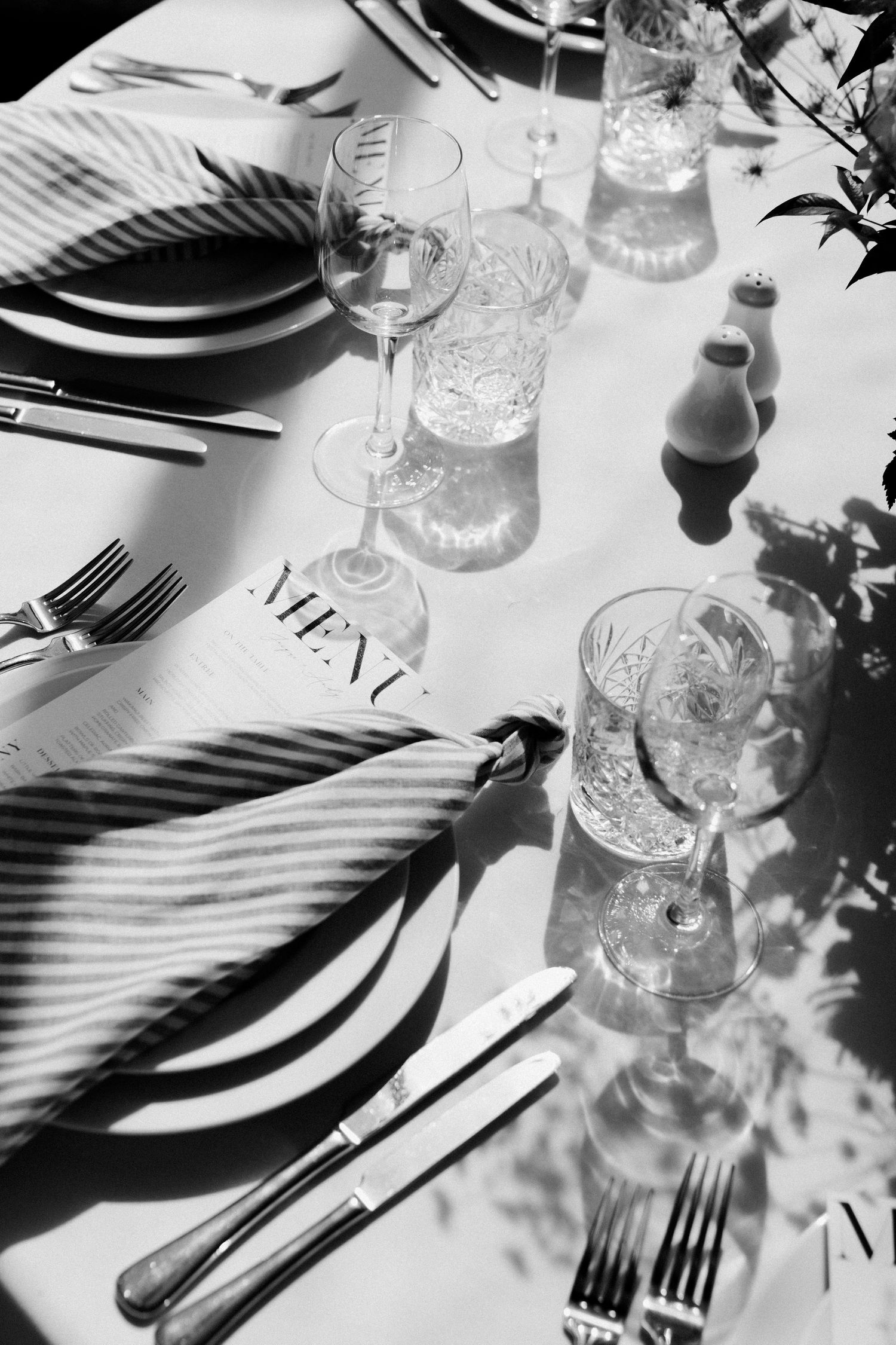 Elegant black and white table setting with crystal glasses and striped napkins at wedding reception.