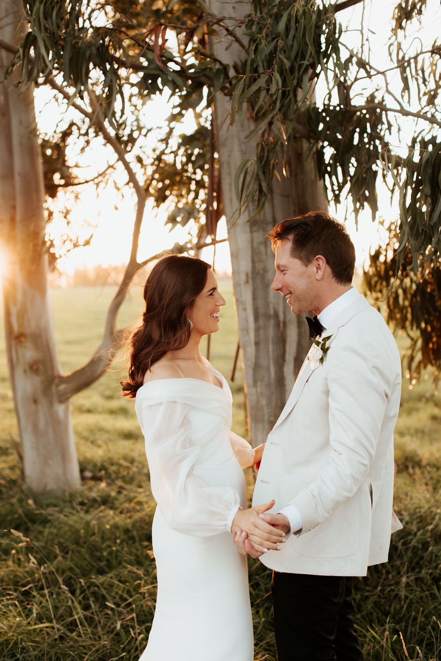 Newlyweds share an intimate moment at sunset among eucalyptus trees.