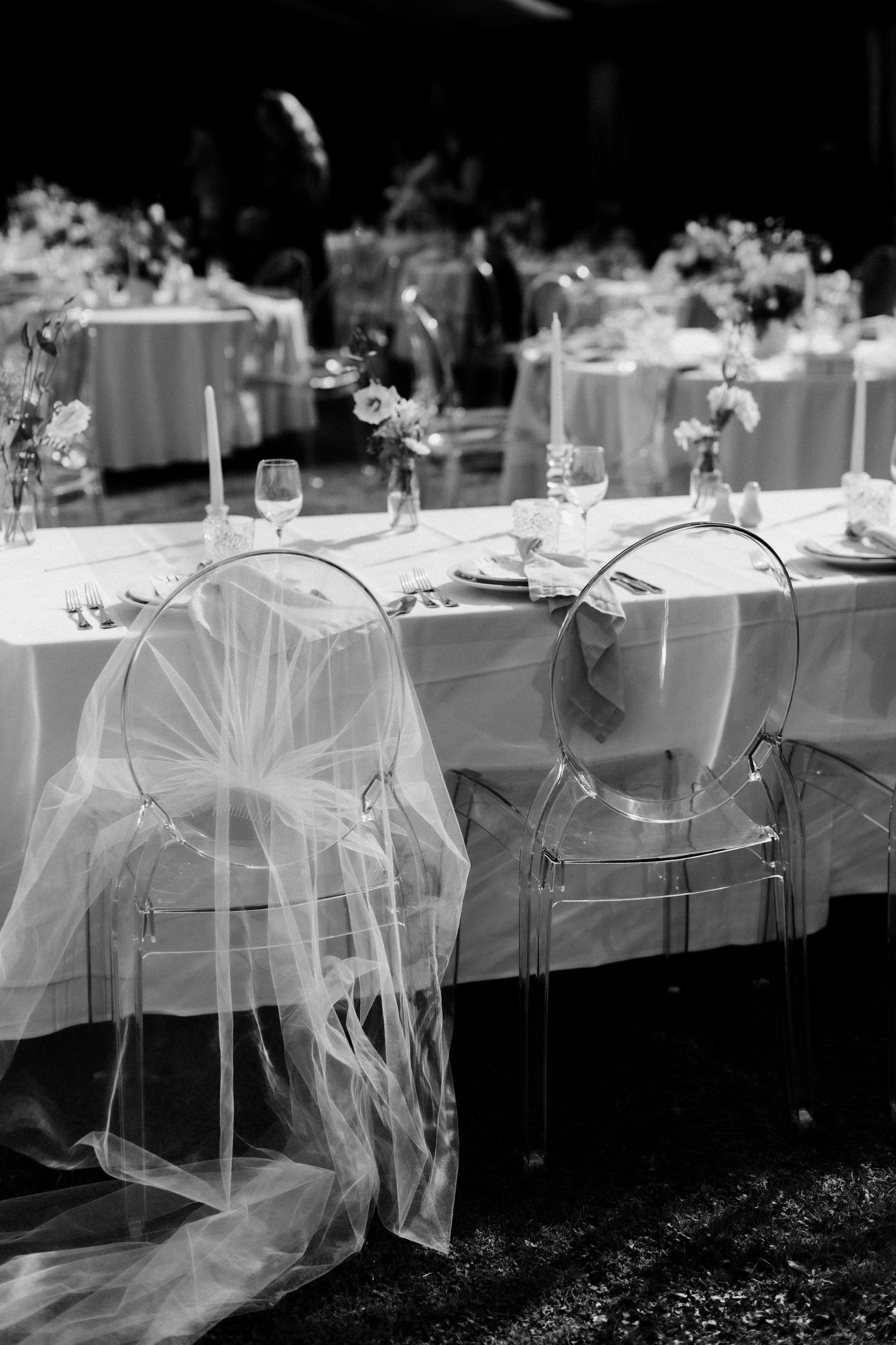 Black and white photo of wedding reception tables with transparent ghost chairs and tulle decorations.