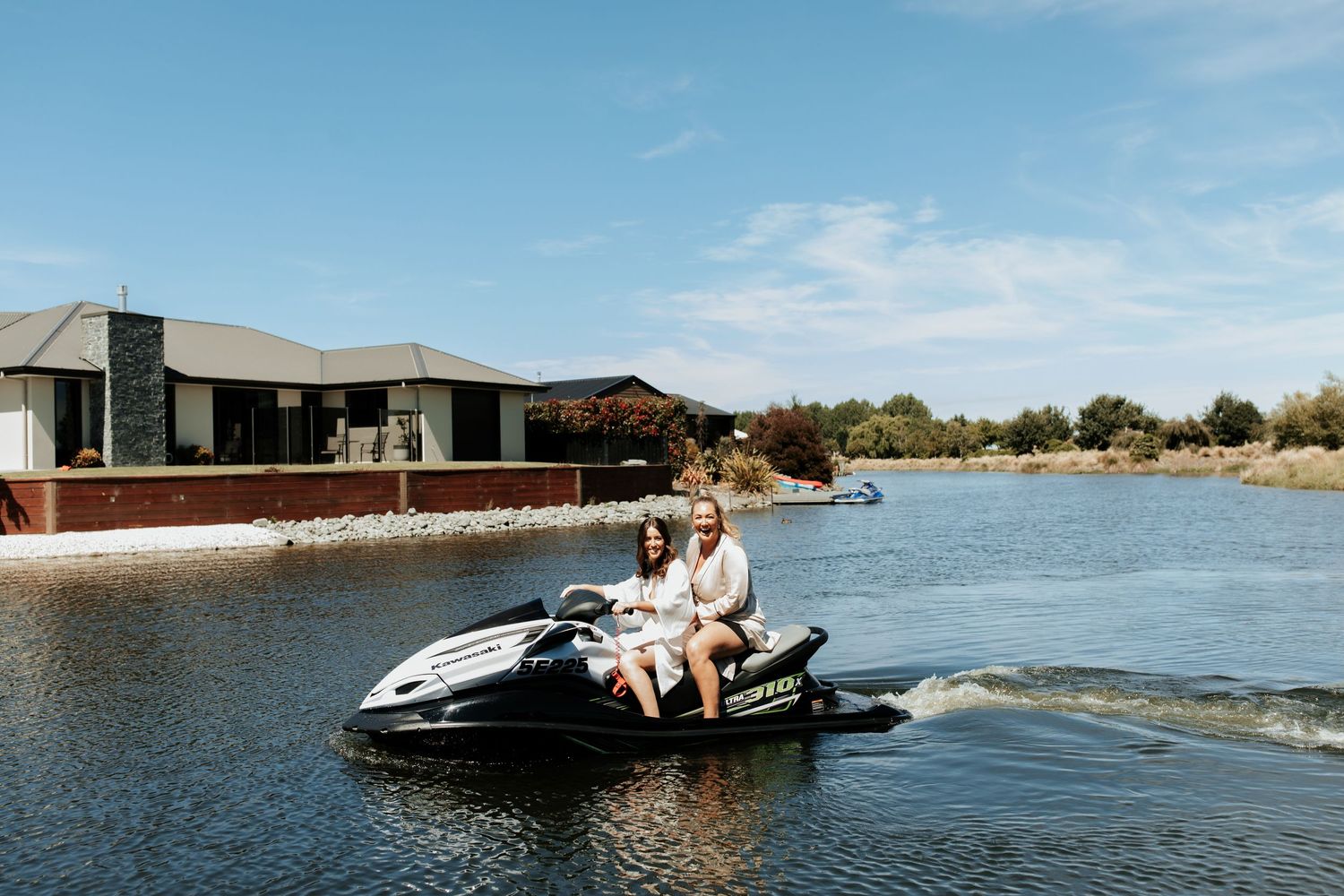 People riding jet ski on lake with modern house in background.