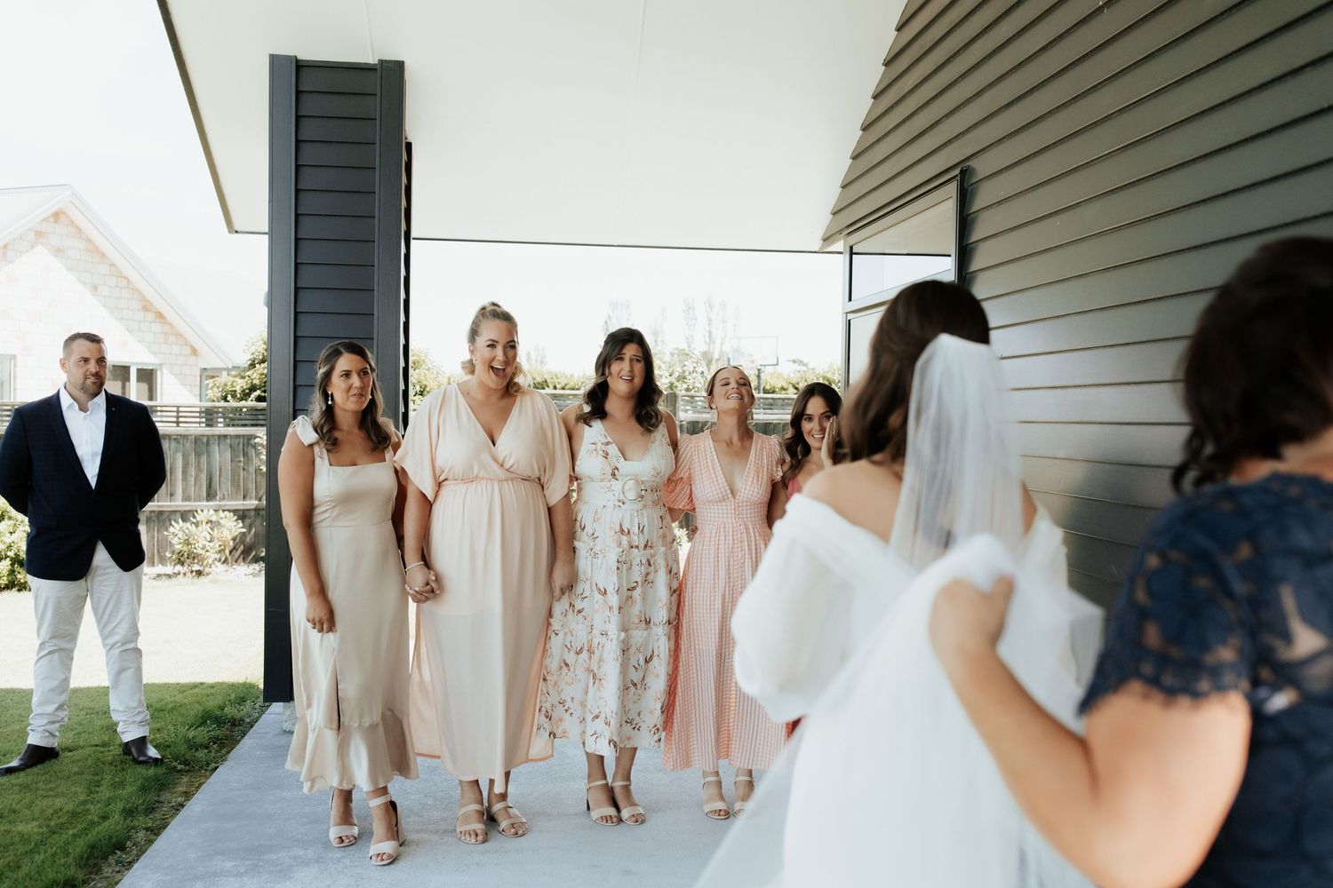 Wedding party wearing pastel dresses walking on outdoor porch.