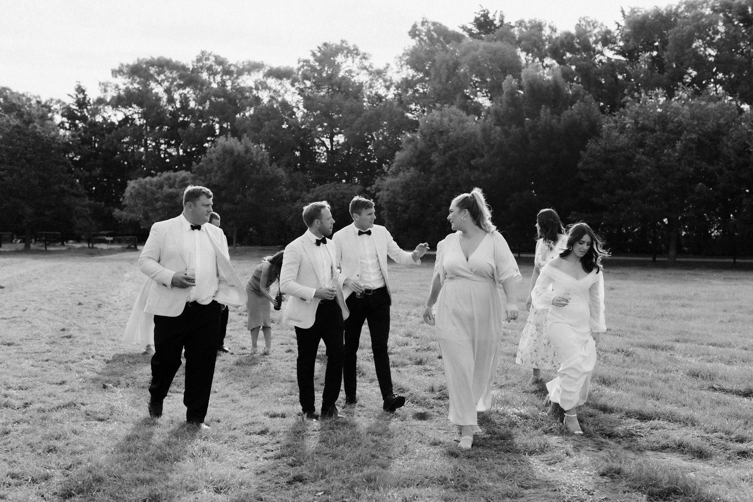 A black and white photo of wedding party members running joyfully across a field.