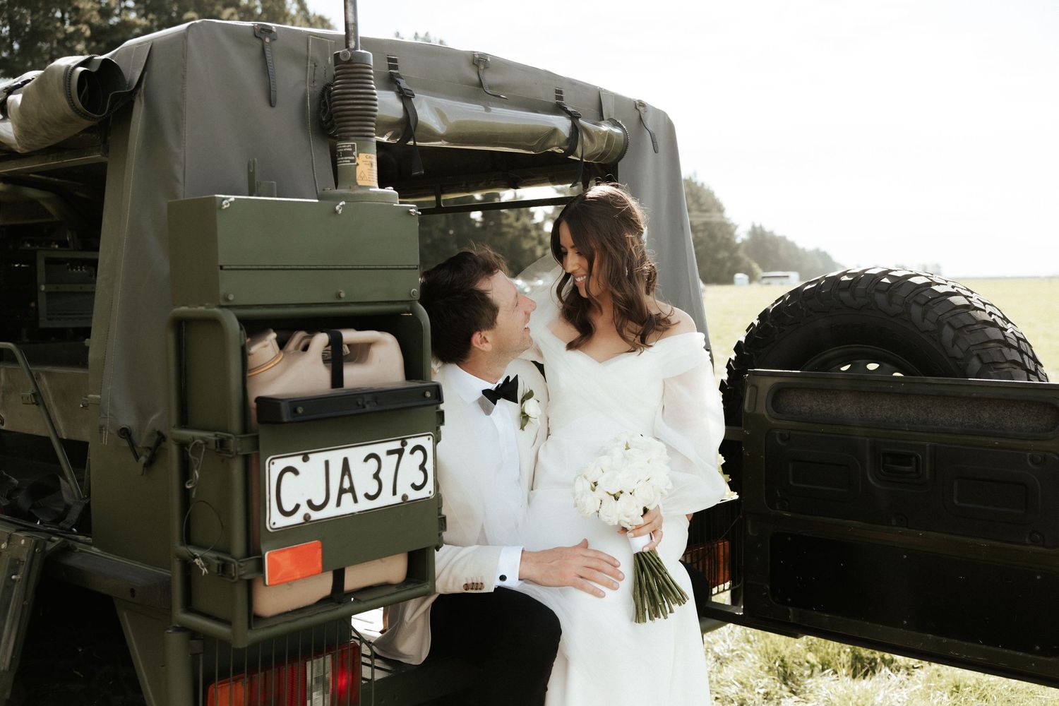 A couple shares an intimate moment in front of a vintage military vehicle on their wedding day.