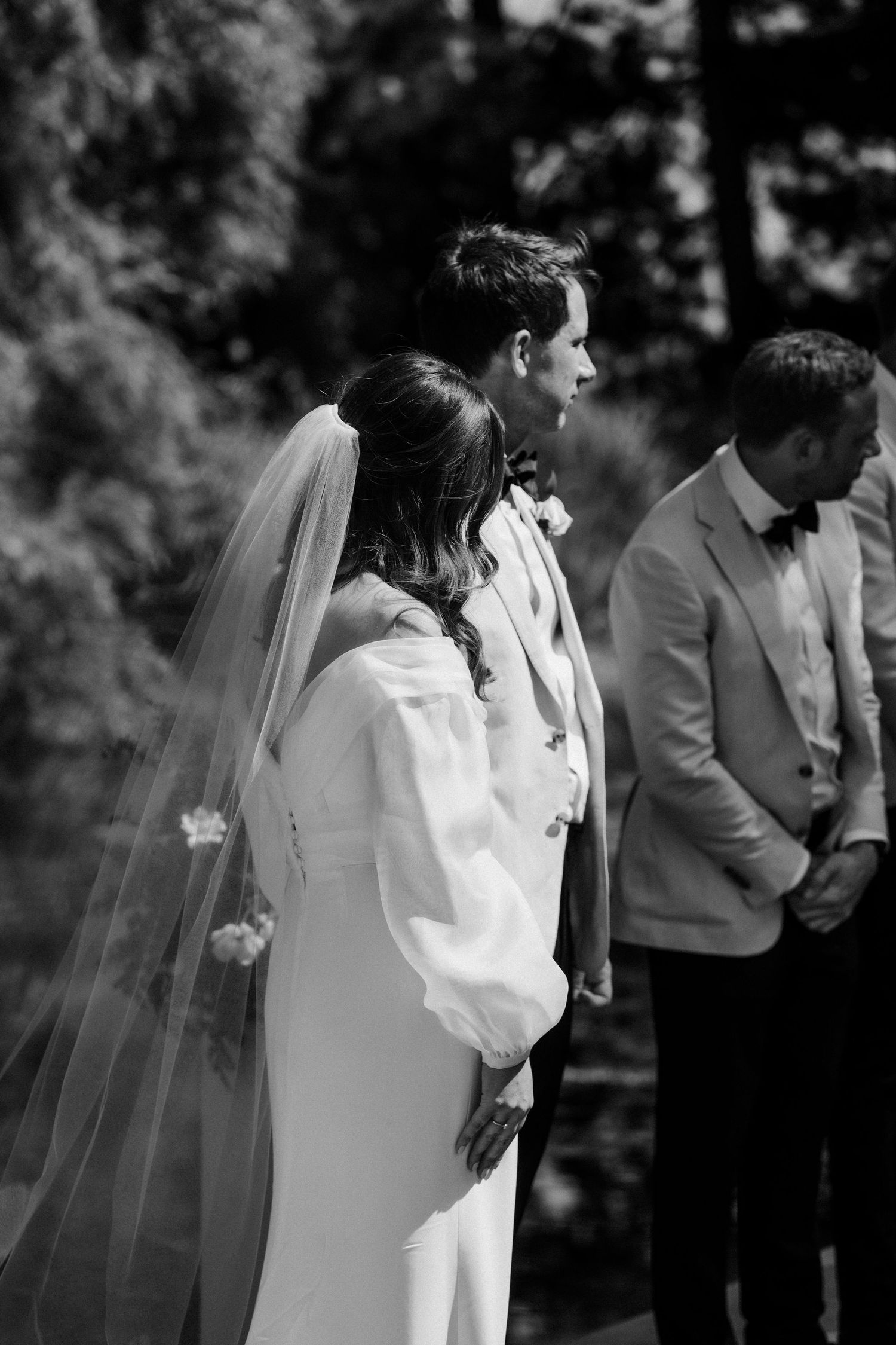 Black and white photo of wedding party standing during outdoor ceremony.