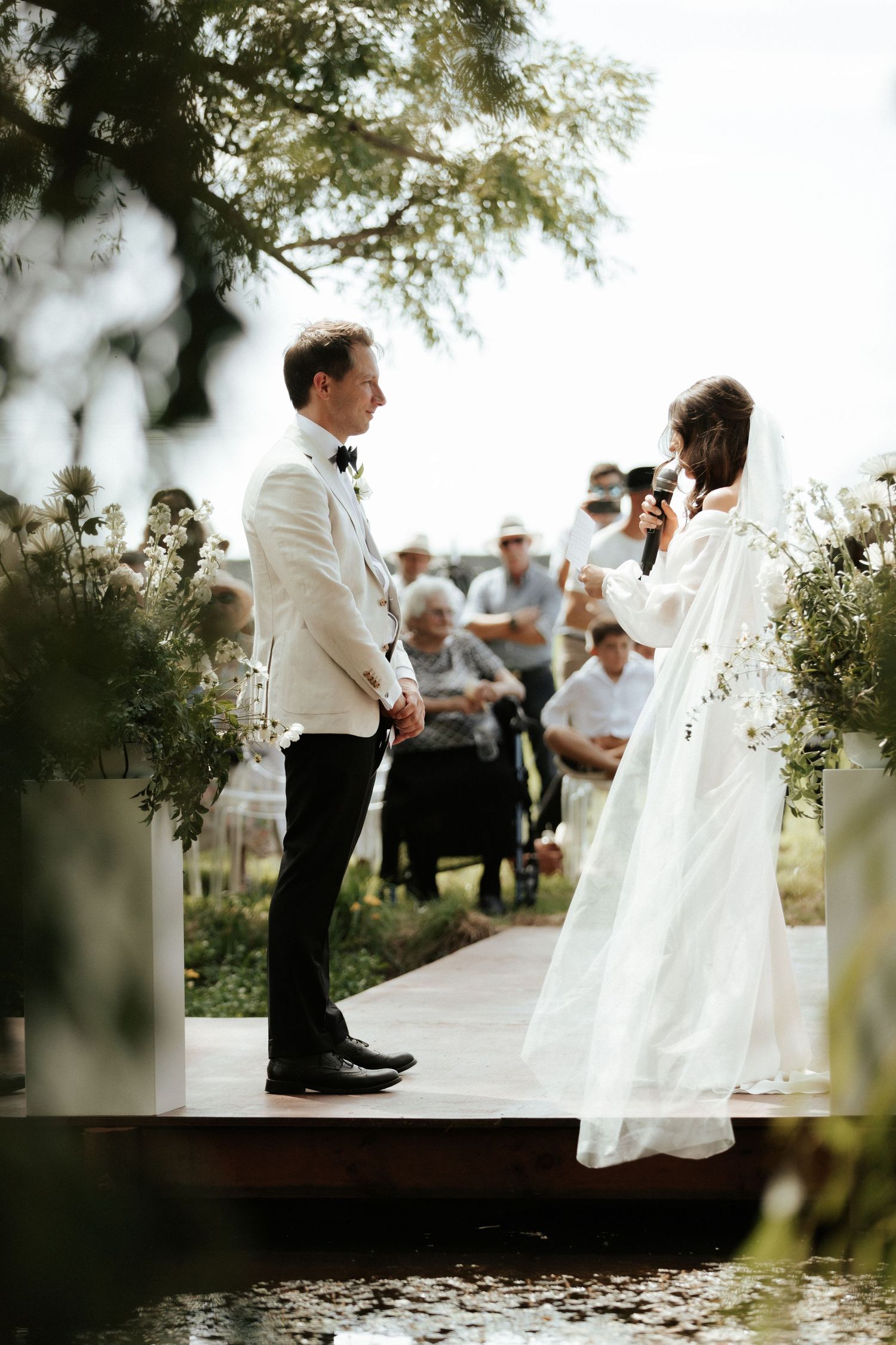 Outdoor wedding ceremony with guests watching as vows are exchanged on a wooden platform.