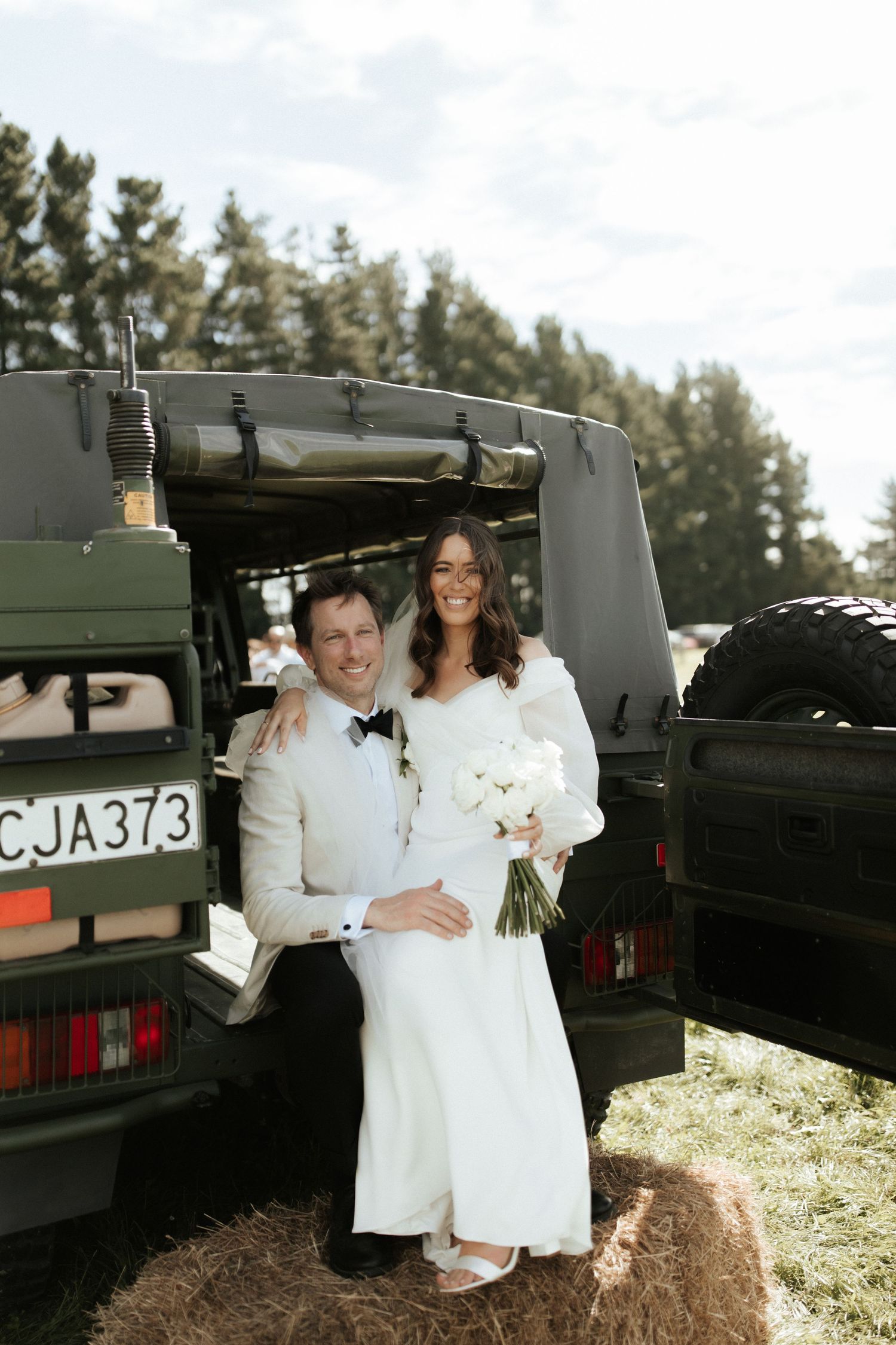 Happy newlyweds pose together against a military vehicle outdoors.