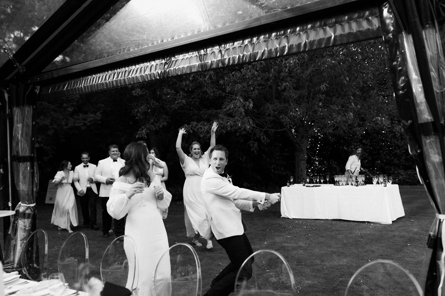 Black and white photo of wedding guests dancing under a covered outdoor venue.