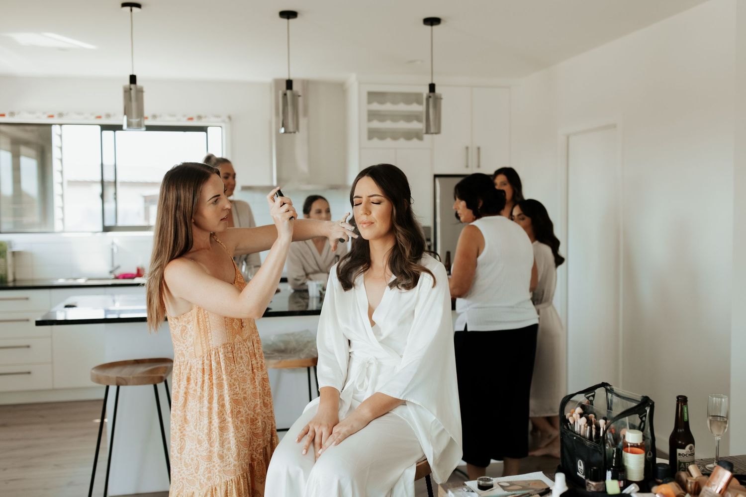 Wedding preparation scene in modern white kitchen with pendant lights.