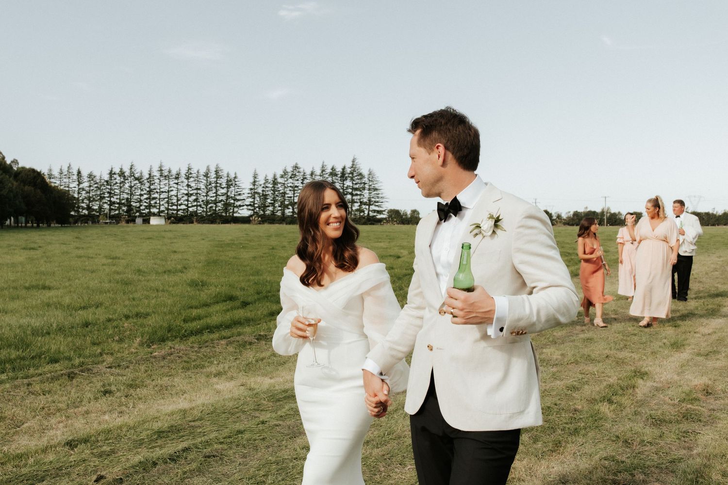 Newlyweds walking together across a green field during sunset celebration.
