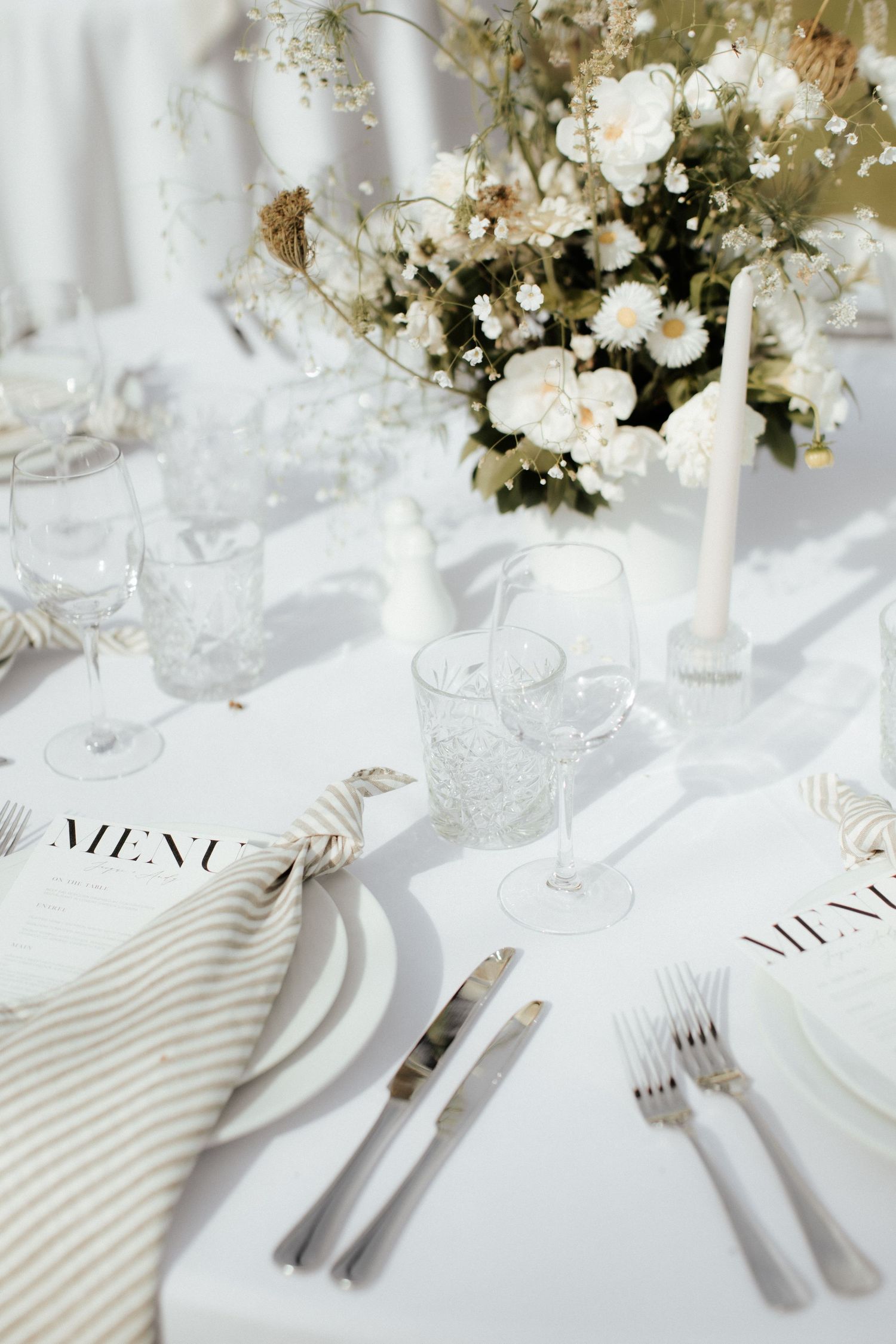 Close-up of white wedding table setting with striped napkin, menu card and crystal glassware.