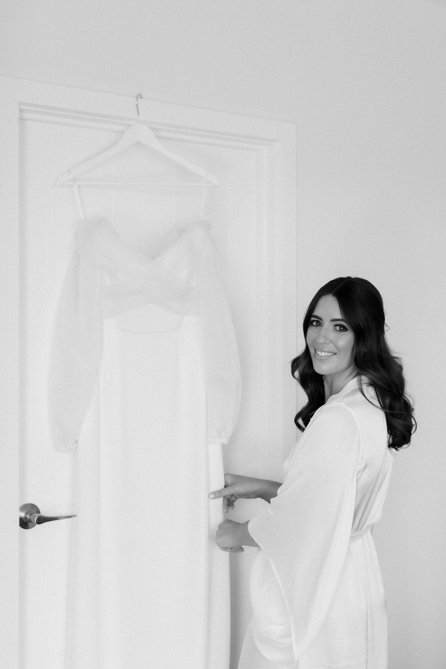 Wedding preparation scene with white dress hanging on door.