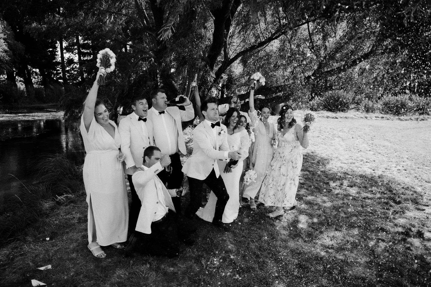 Black and white photo of wedding party posing playfully outdoors.