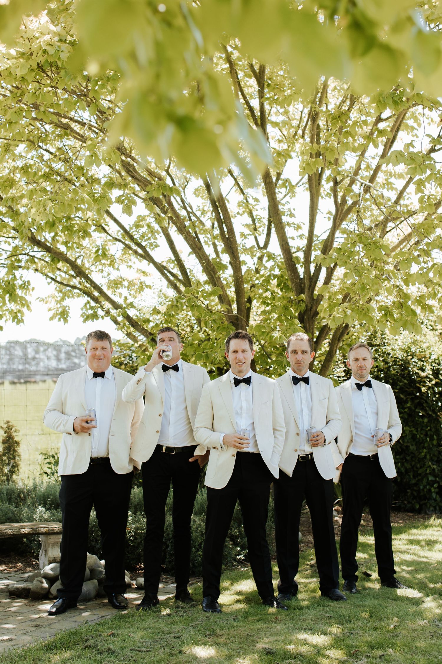 Groomsmen in white dinner jackets posing under a blooming tree.