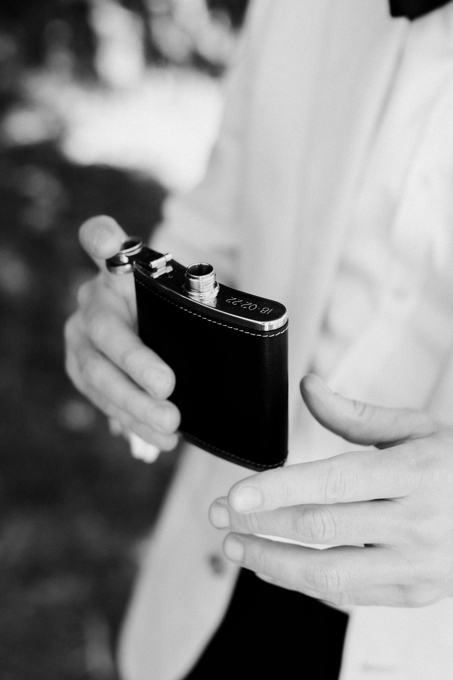 Hands holding a black leather flask against formal attire.