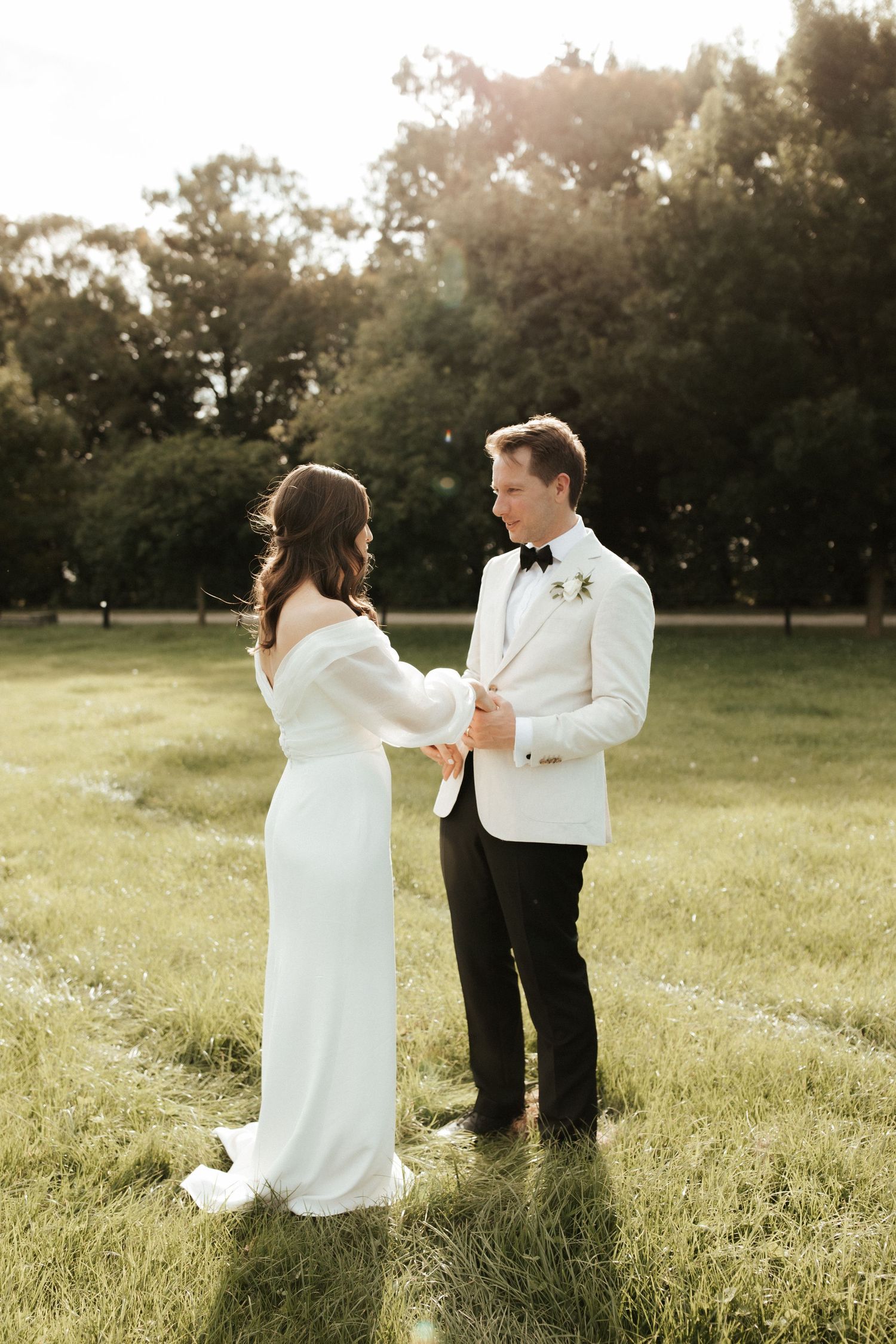 A couple shares a romantic moment at sunset in a grassy field with trees in the background.