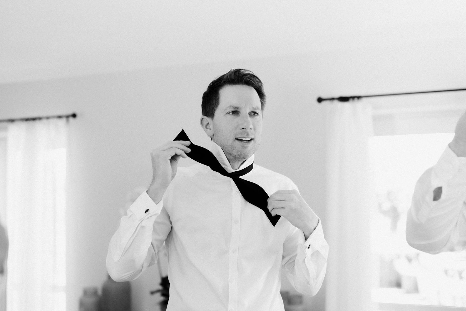 Person adjusting black bowtie while wearing white dress shirt.