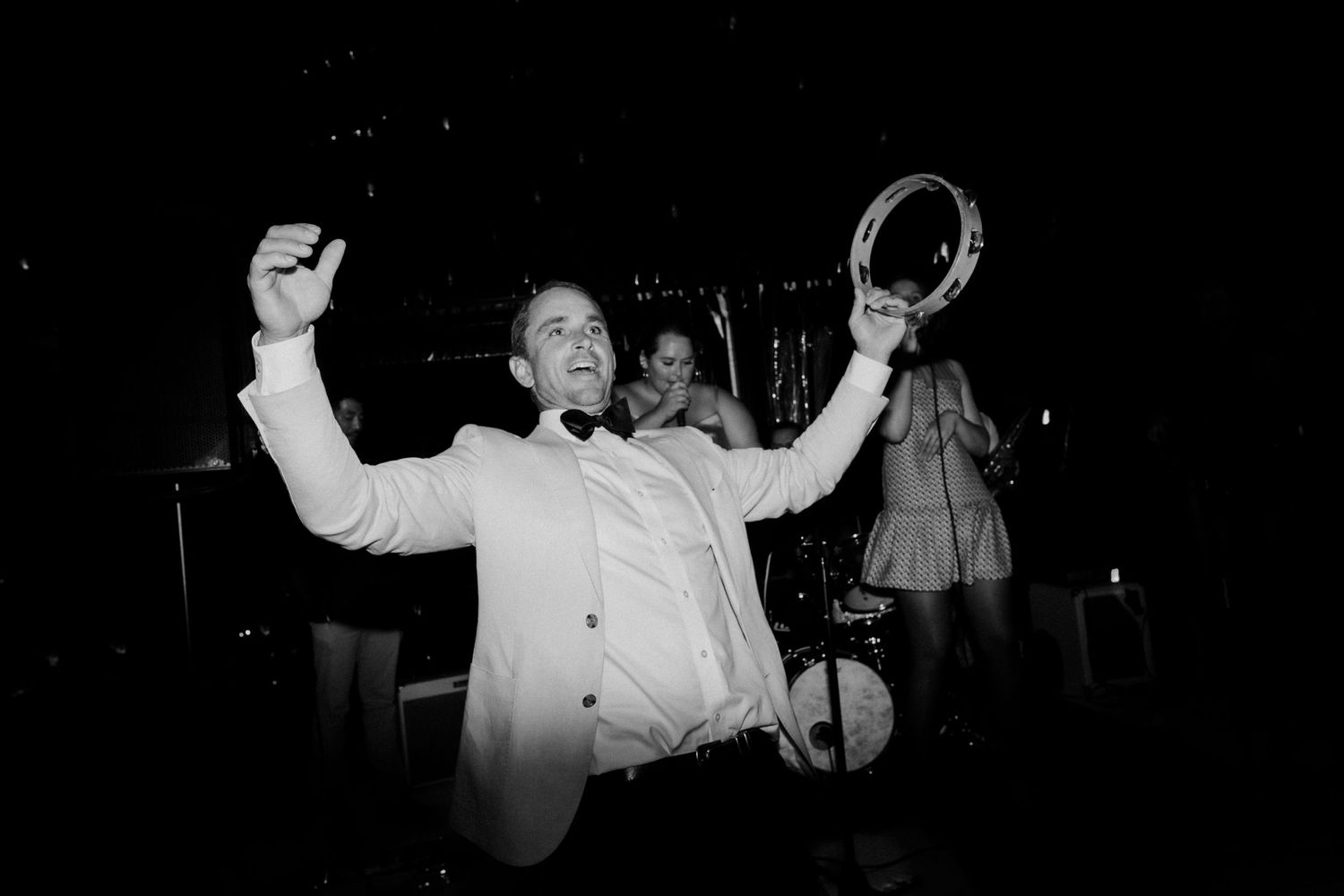 Person in white jacket celebrates with raised arms at nighttime event.