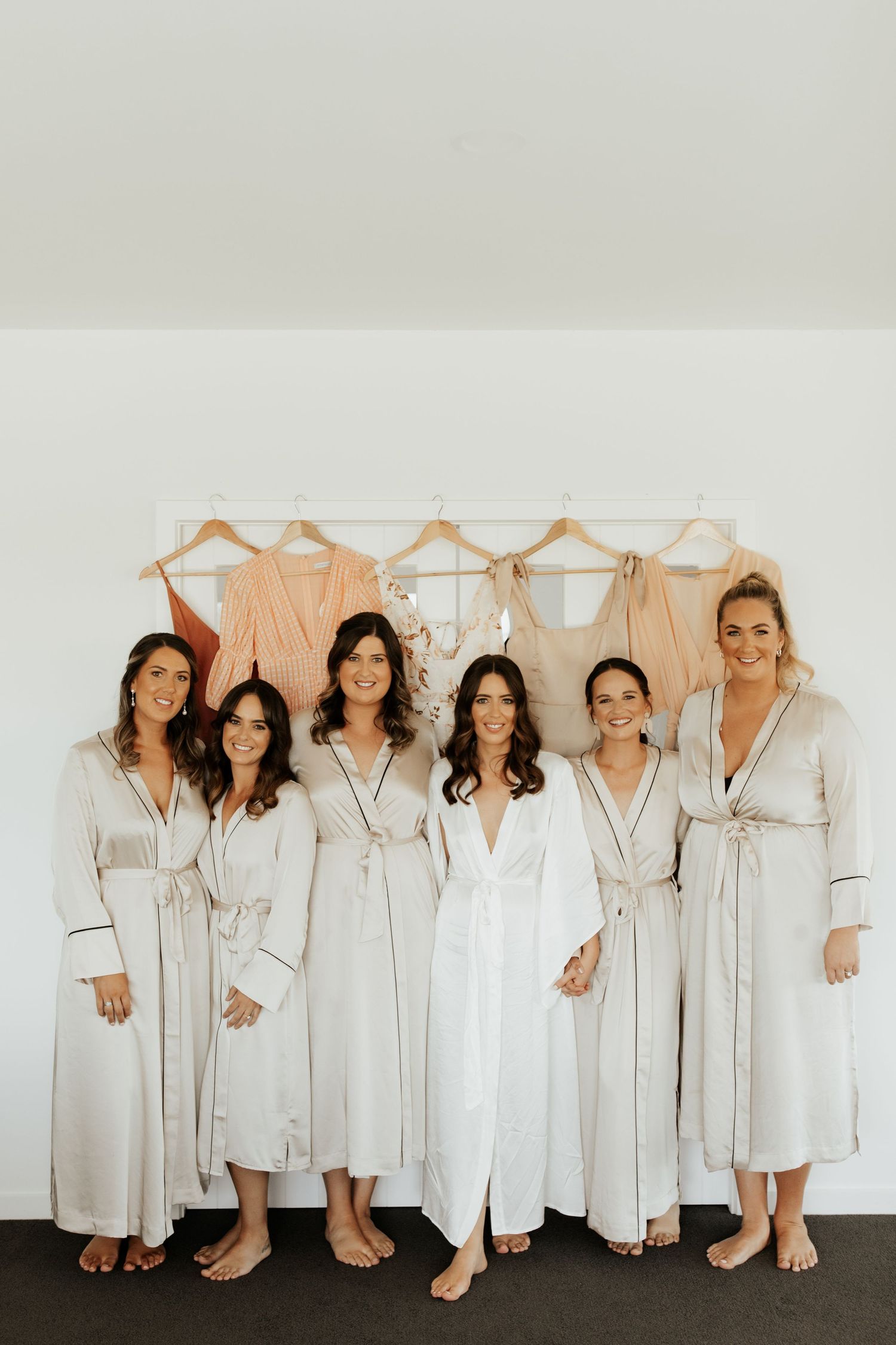 Group wearing matching light colored robes posing together against a wall with hanging garments.