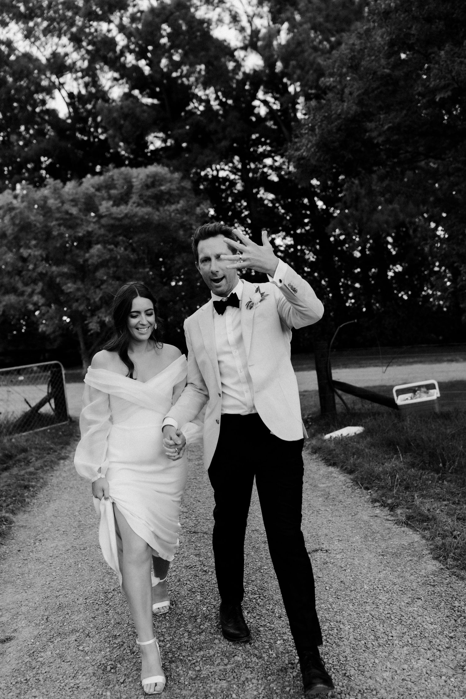 Joyful couple in wedding attire dancing on a garden path.