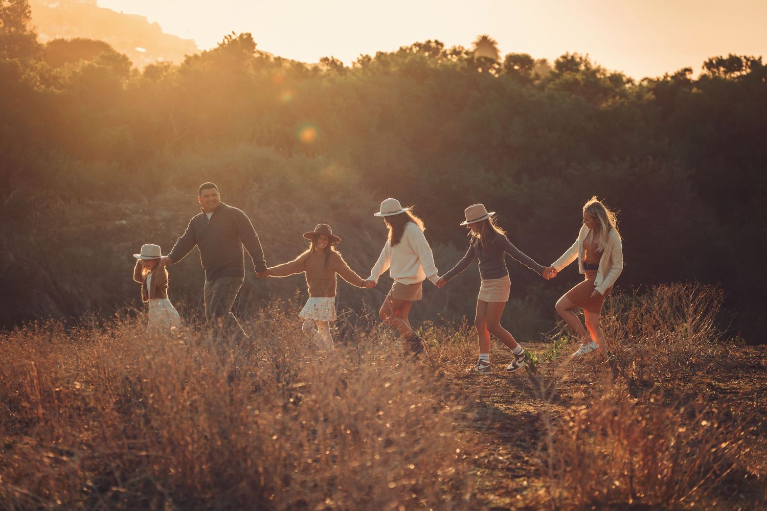 A group walks hand in hand through a golden field at sunset.