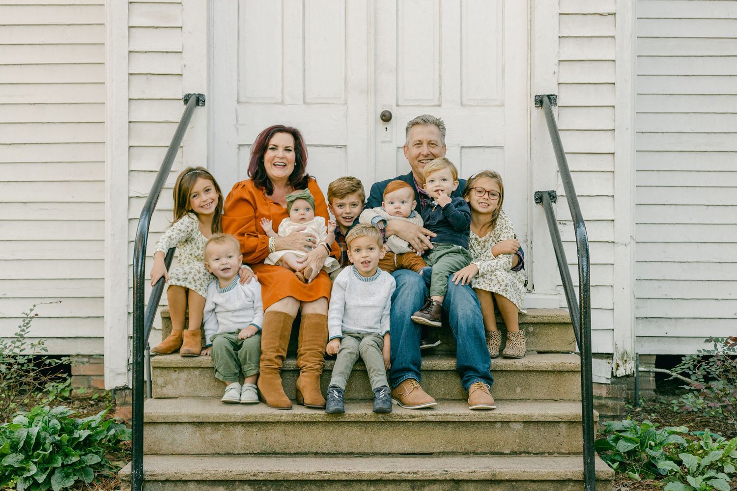 grandparents sit on the steps of a church, surrounded by eight grandchildren