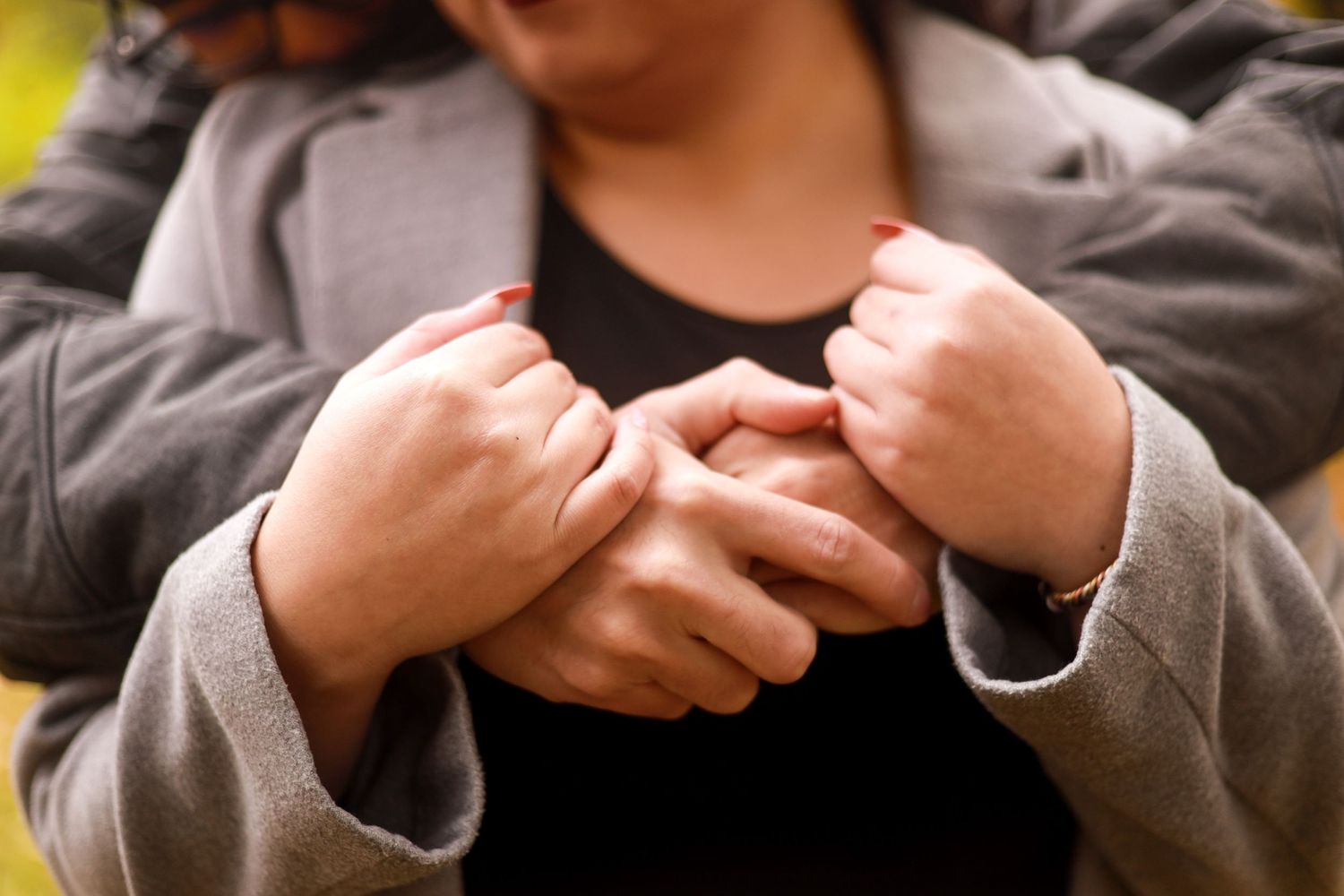 Close up of hands clasped together over a grey sweater showing intimacy and connection.