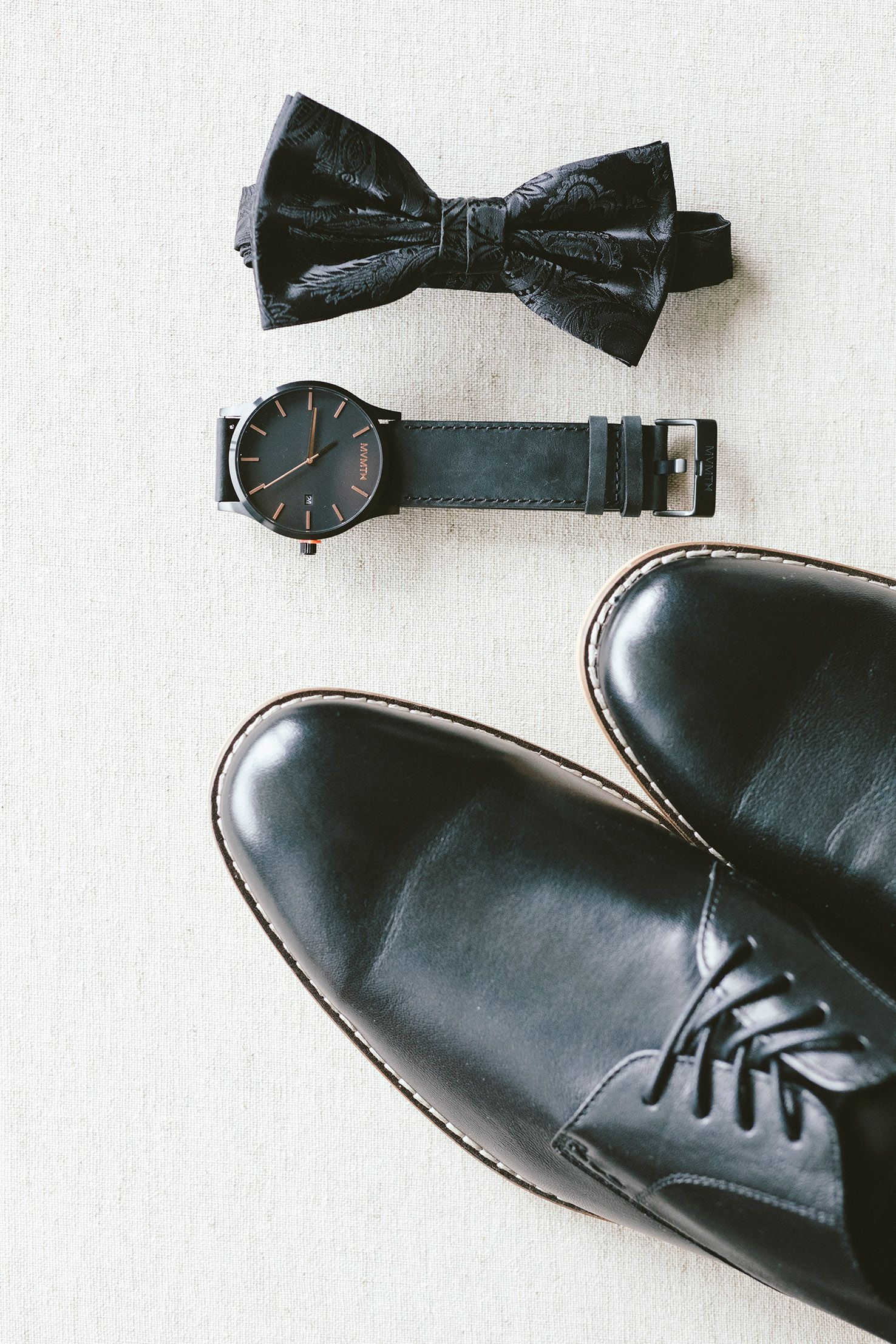 Black dress shoes and bow tie arranged on a white surface.