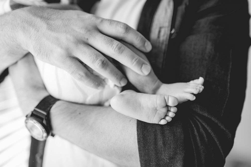 Close-up black and white photo of parent's hands gently touching newborn baby's feet.