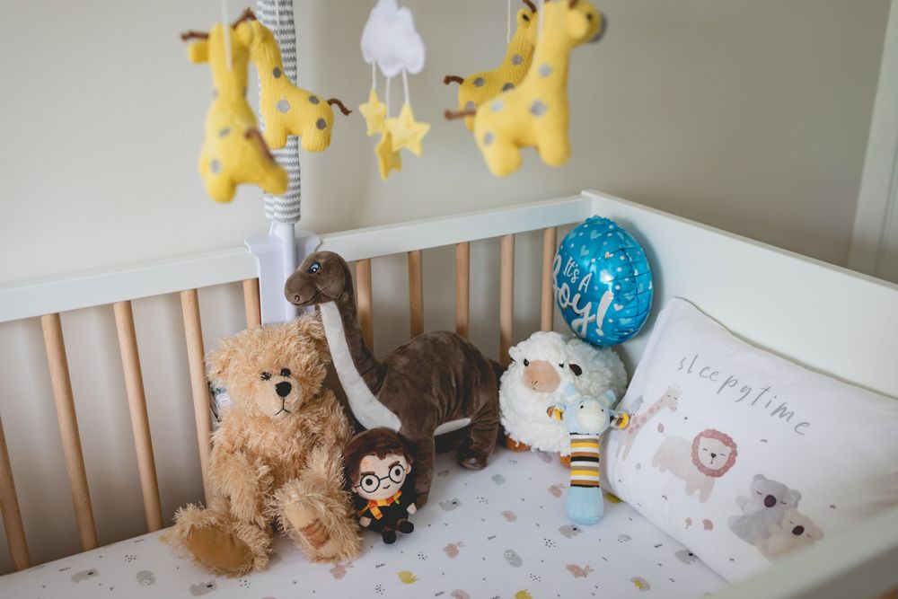 Nursery crib with stuffed animals and yellow giraffe mobile above.