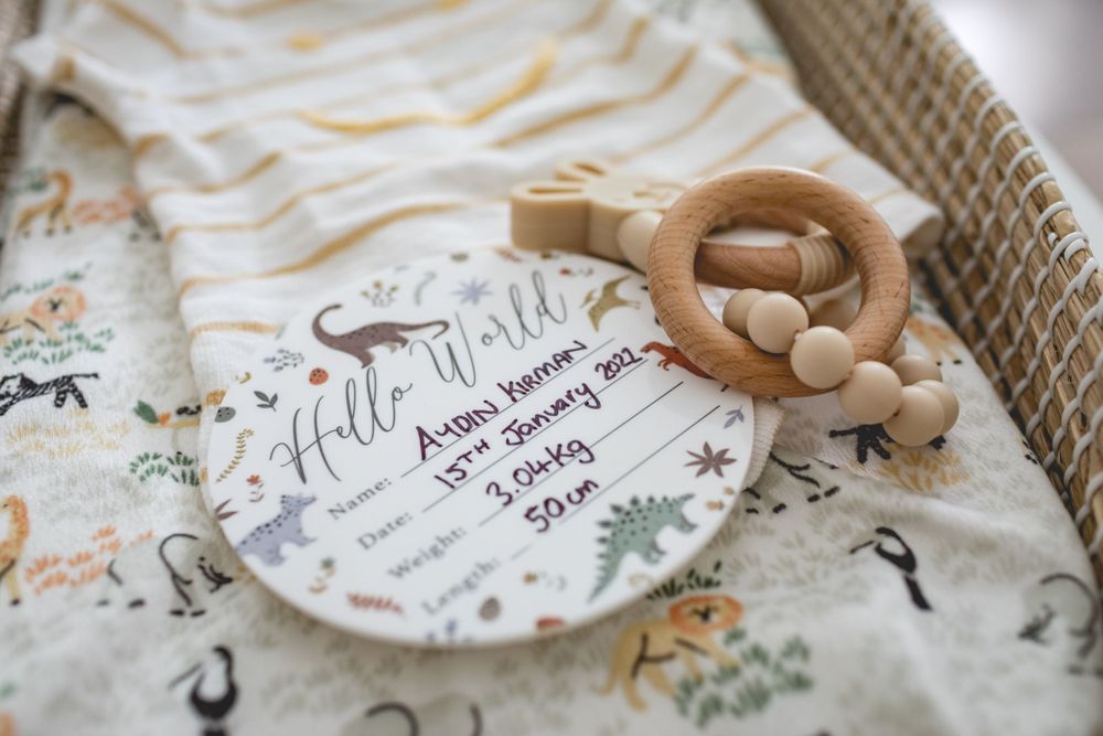 Wooden teething toy on floral patterned fabric with milestone celebration plate.
