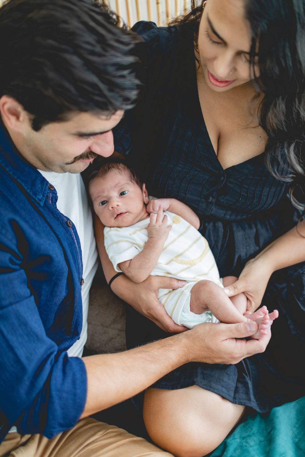 Tender family moment with newborn baby wrapped in white on bed.