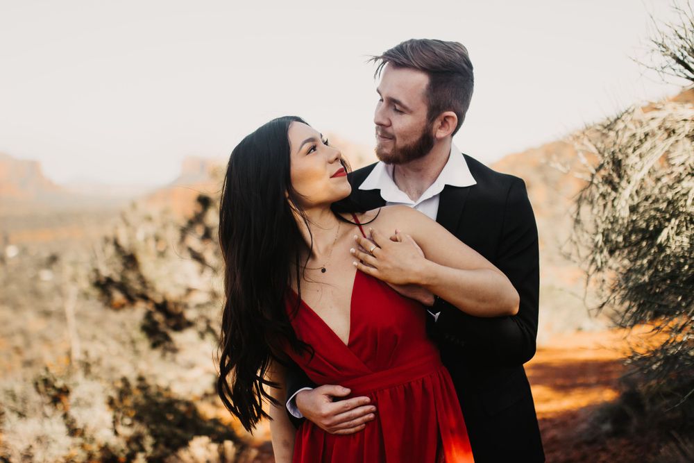 A couple shares an intimate moment in formal attire against a warm desert setting.