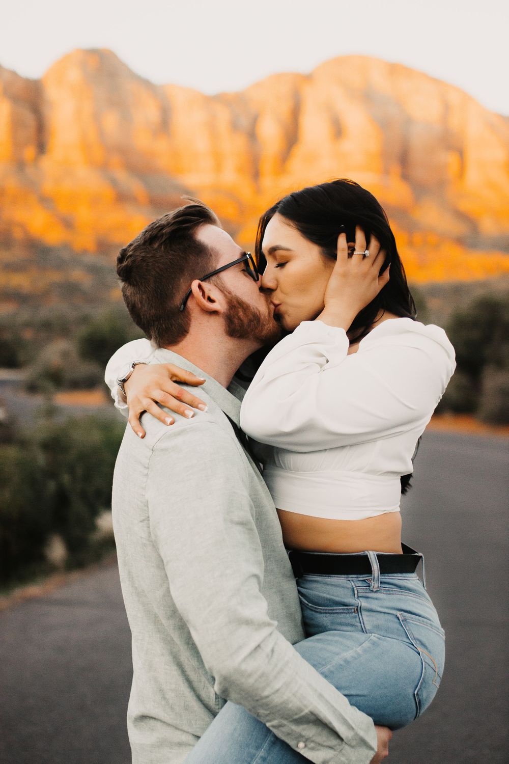 Intimate couple embraces during sunset photoshoot with red mountains in background.