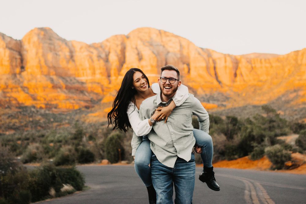 Playful engagement session on desert road with mountains glowing at sunset.