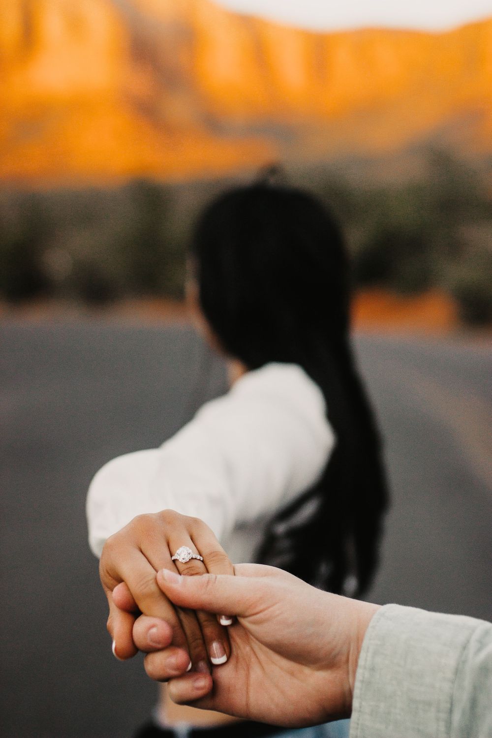 Close-up of engagement ring with desert mountains glowing orange in background.