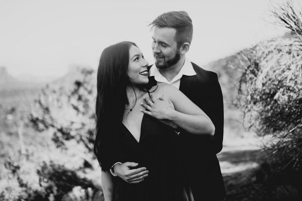 A black and white portrait of a couple in an affectionate embrace outdoors.