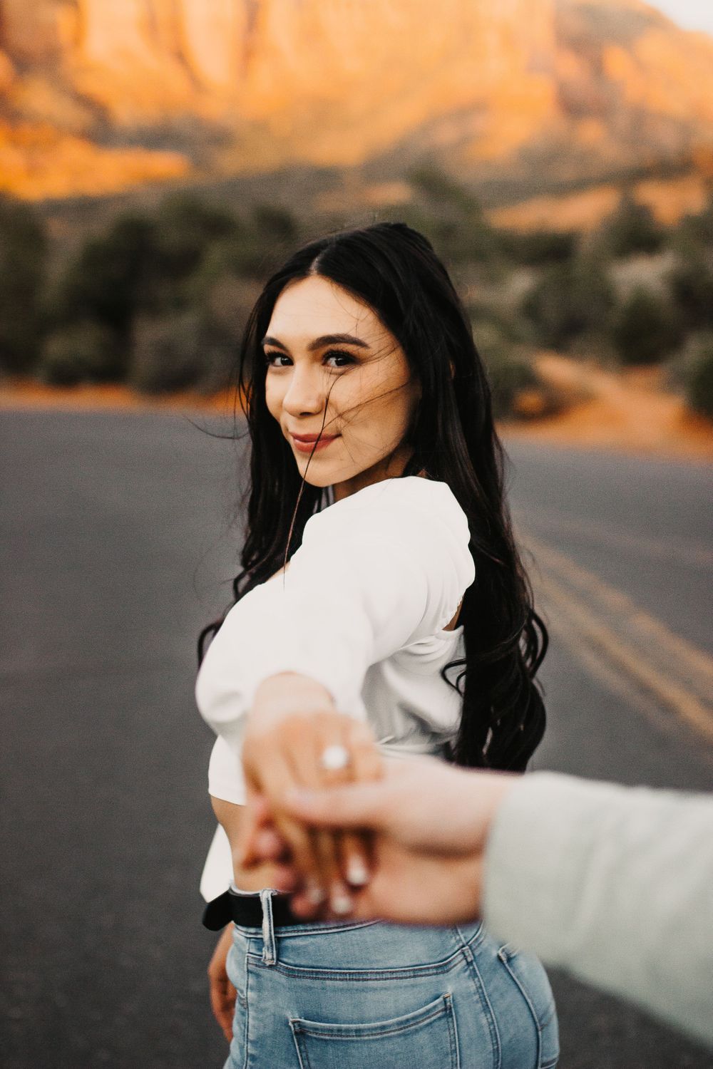 A couple stands together against stunning red rock cliffs during golden hour sunset.