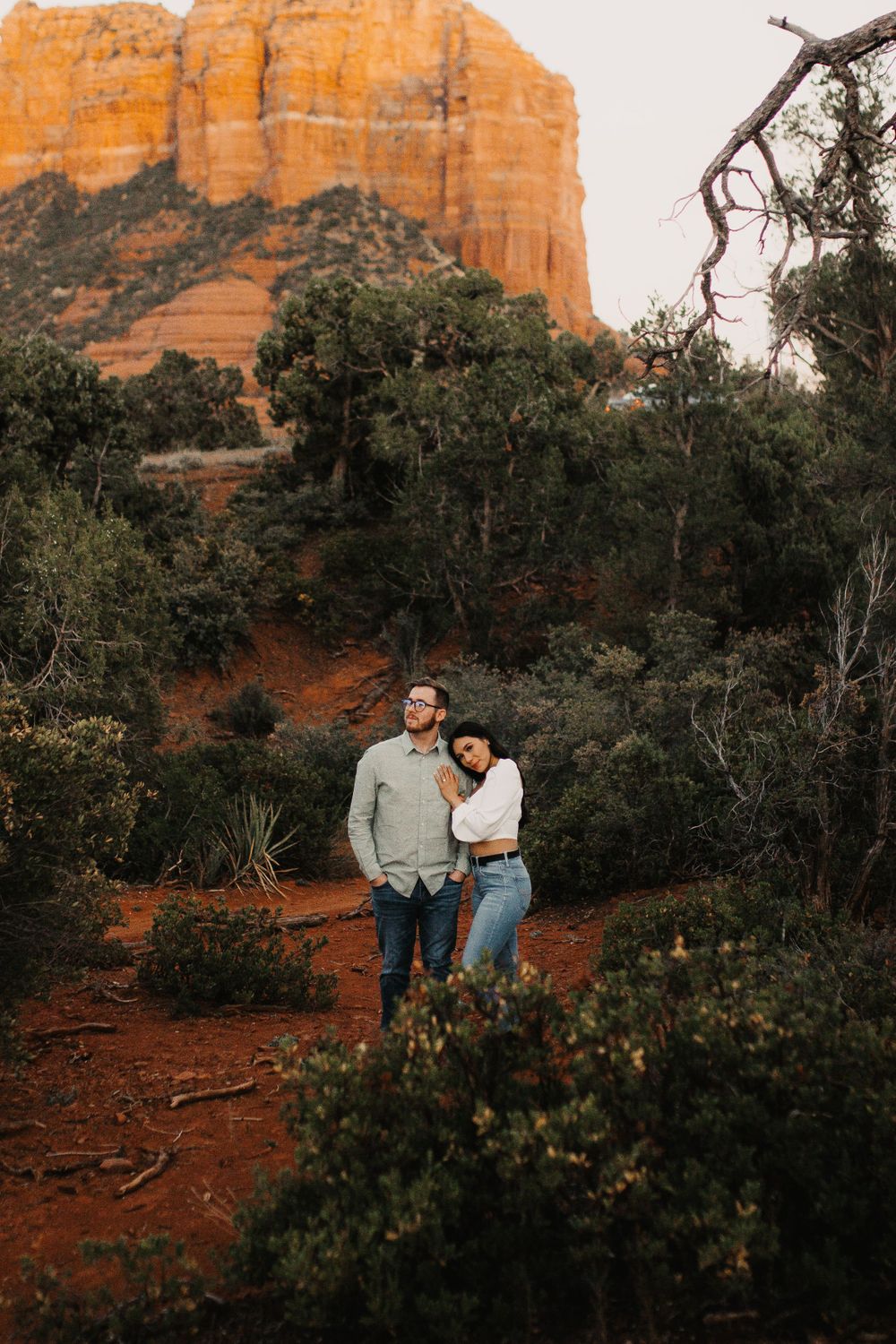 Couple embracing near towering red rock formations during sunset.