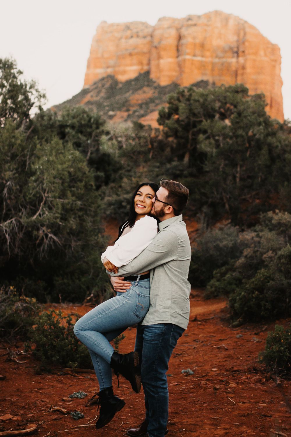A couple embraces against the backdrop of majestic red rock formations during golden hour in Sedona.