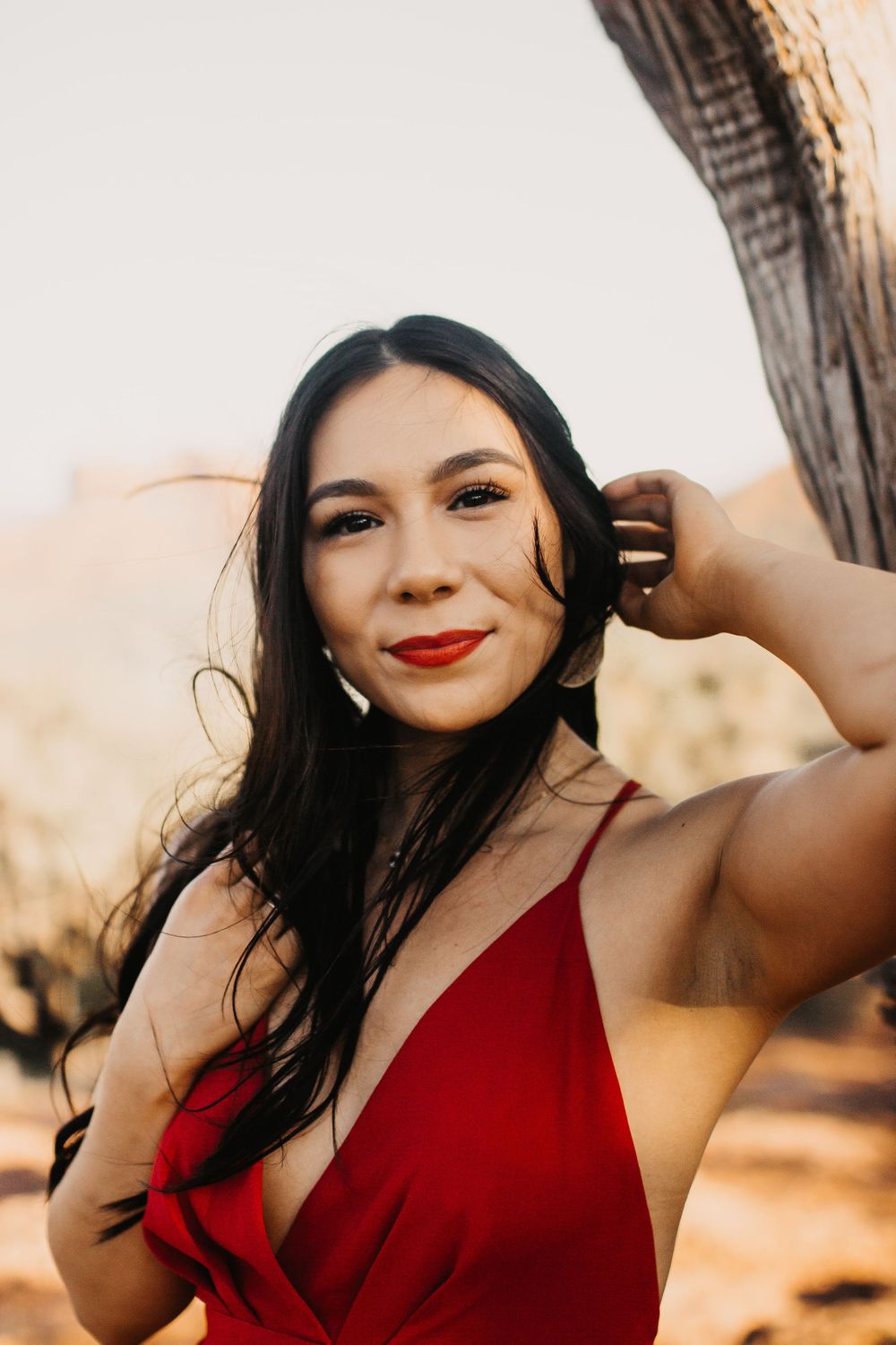 A woman in a red dress poses confidently against a desert landscape.