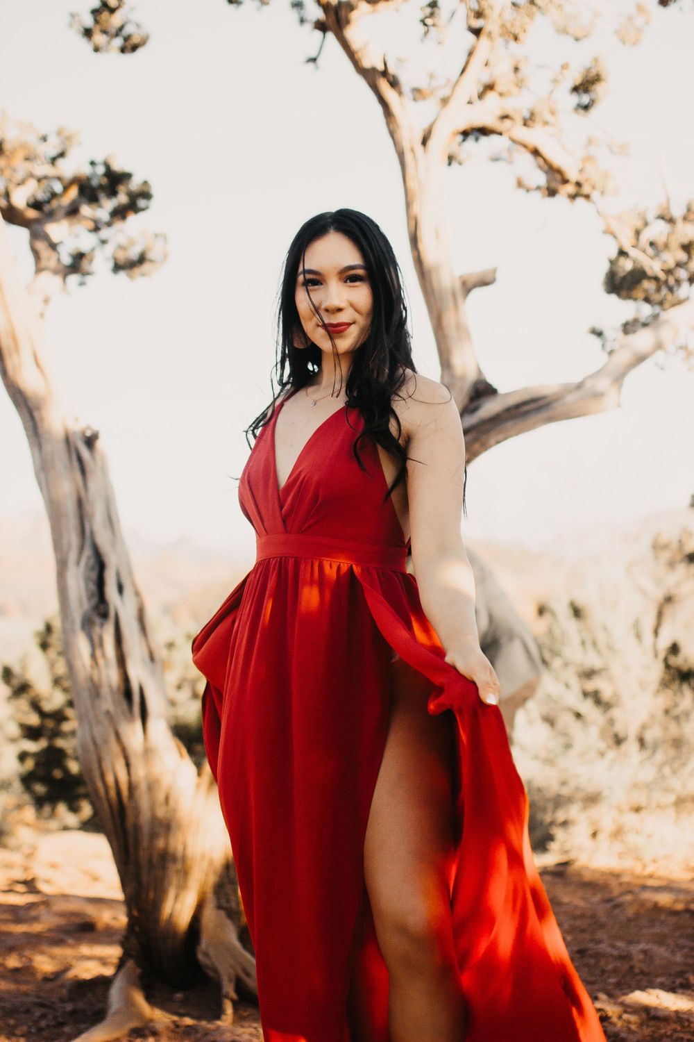 A woman in a vibrant red dress twirls playfully among desert trees.