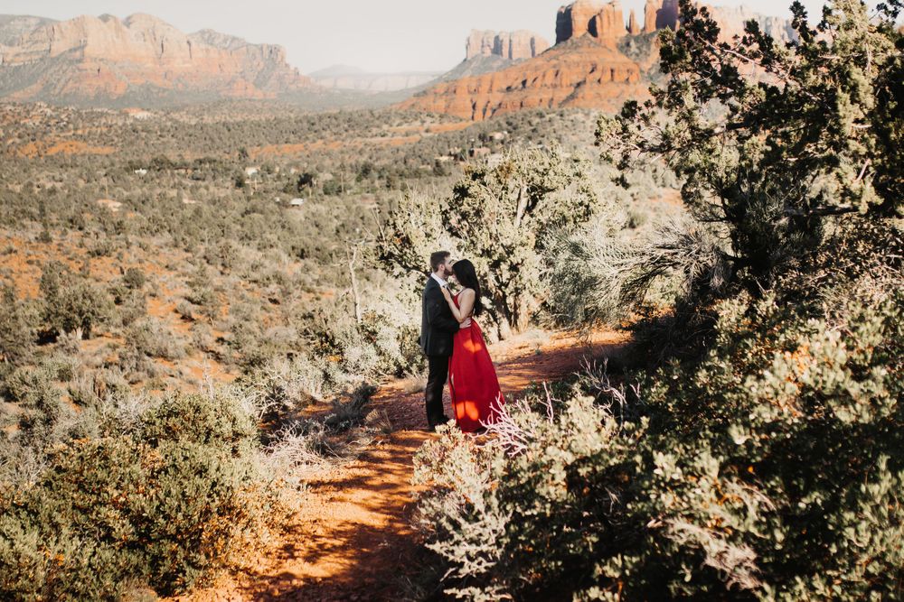 A person in a red dress stands on a scenic desert trail overlooking red rock formations.