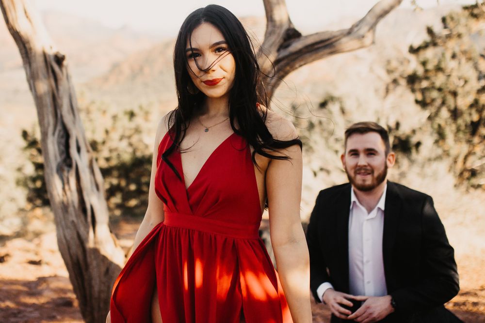 A couple in formal attire poses among desert trees during golden hour.