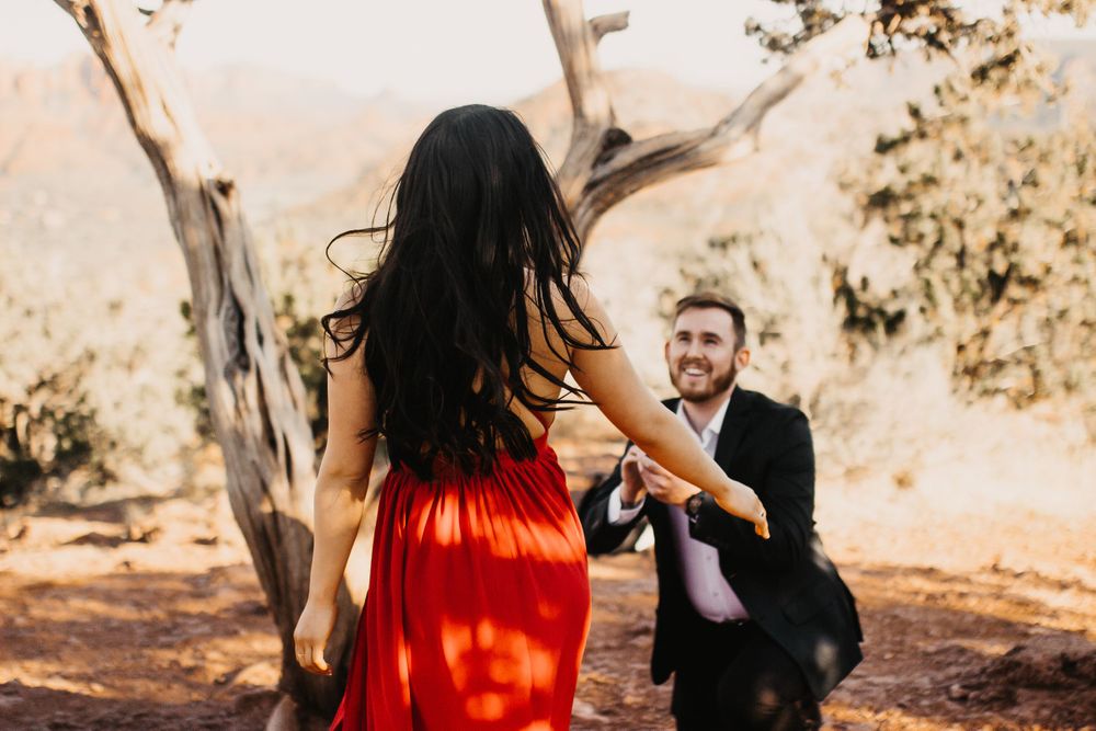 A couple shares a romantic moment in a sunlit outdoor setting with trees in the background.